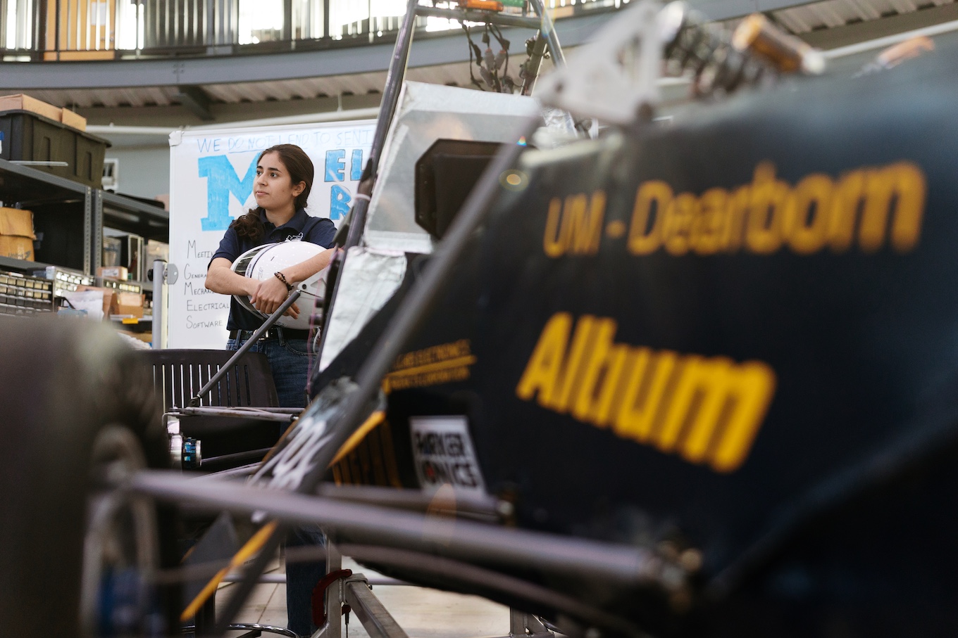 A female student stands in front of a maize and blue electronic race car that students built.