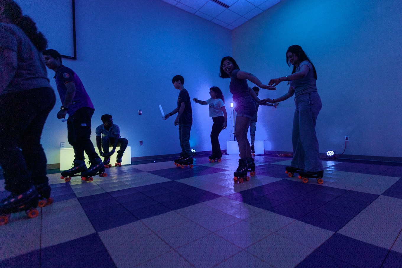 Students roller skate in a blue-lit room 