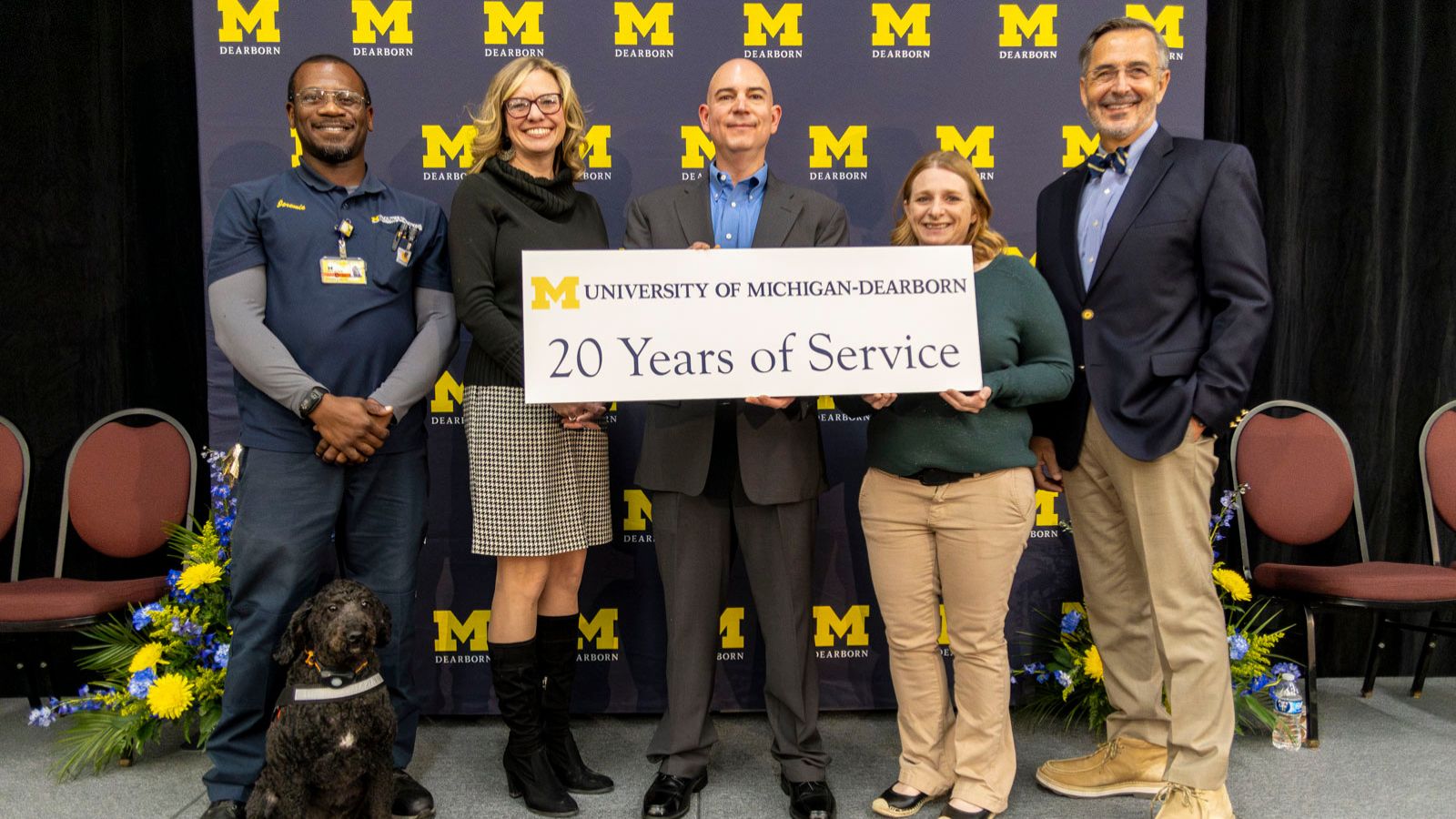 Staff receiving recognition for 20-years of service pictured on stage with Chancellor Grasso in front of a UM-Dearborn background