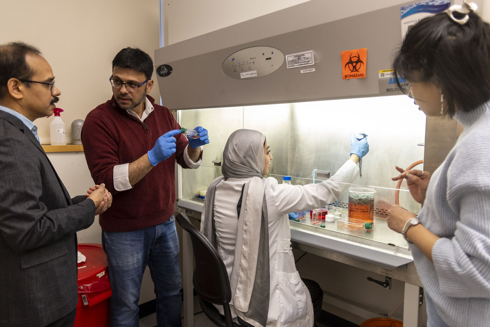 Flanked by microscopes and computers, Associate Professor of Biology Kalyan Kondapalli and Assistant Professor of Physics Suvranta Tripathy work with two female graduate students in a biology lab.