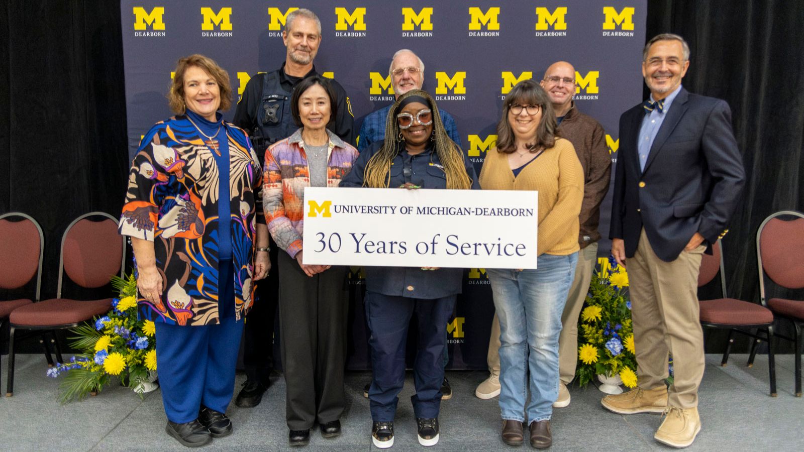 Staff receiving recognition for 30-years of service pictured on stage with Chancellor Grasso in front of a UM-Dearborn background