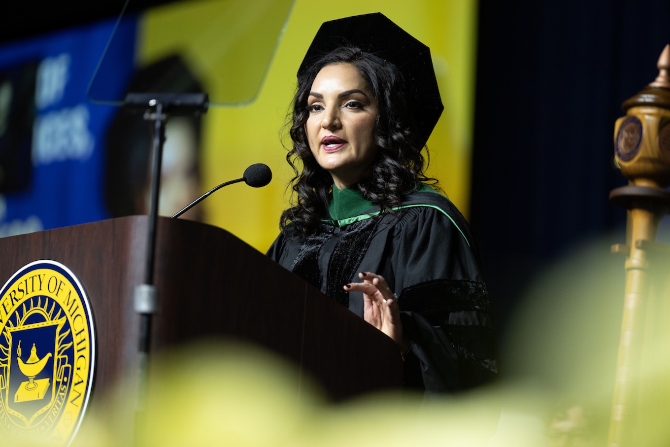 A woman wearing a cap and gown speaks at a graduation ceremony podium