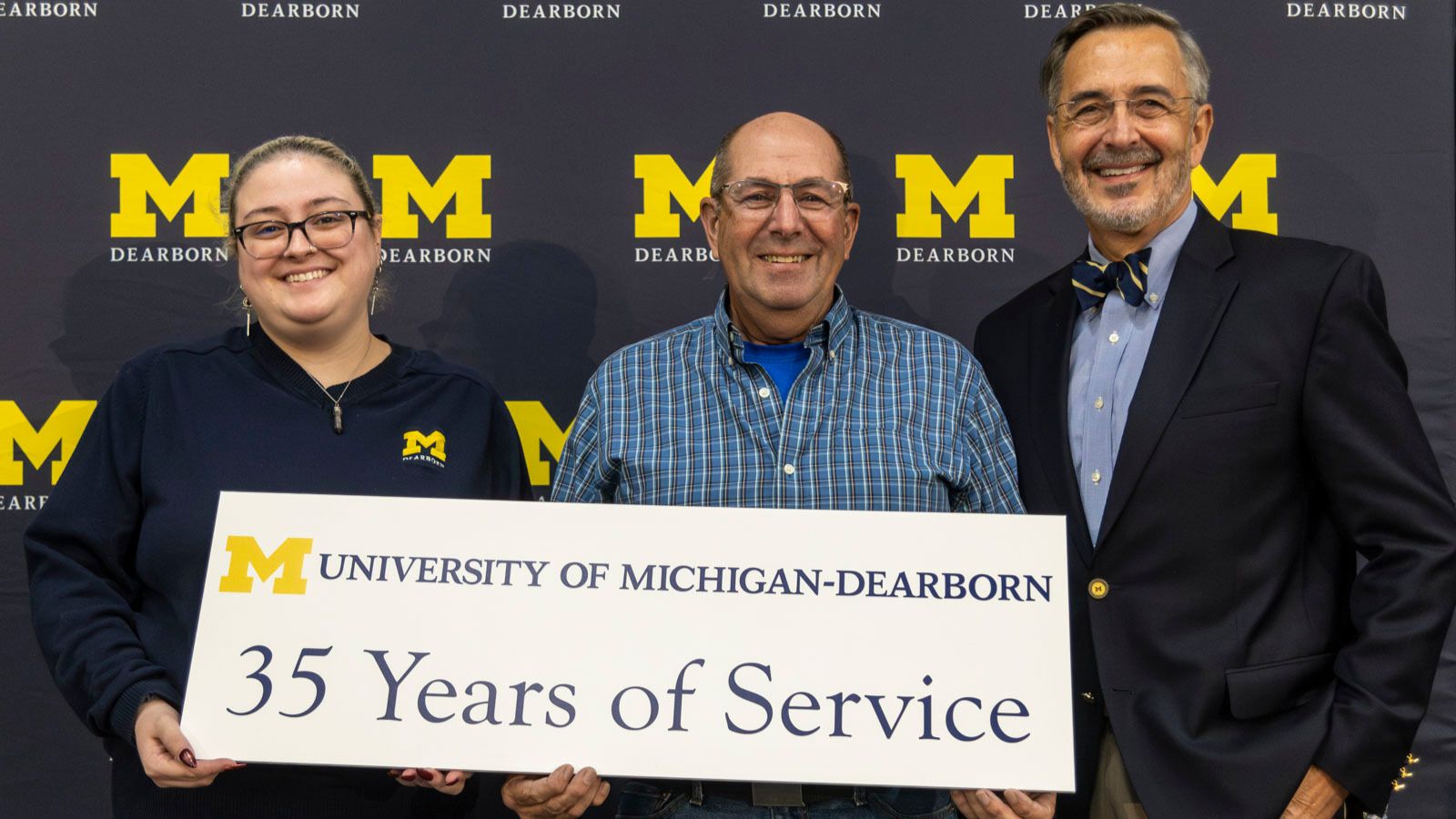 Staff receiving recognition for 35-years of service pictured on stage with Chancellor Grasso in front of a UM-Dearborn background