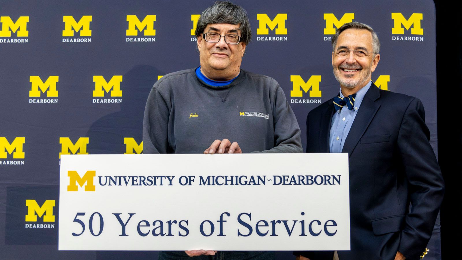 Staff receiving recognition for 50-years of service pictured on stage with Chancellor Grasso in front of a UM-Dearborn background