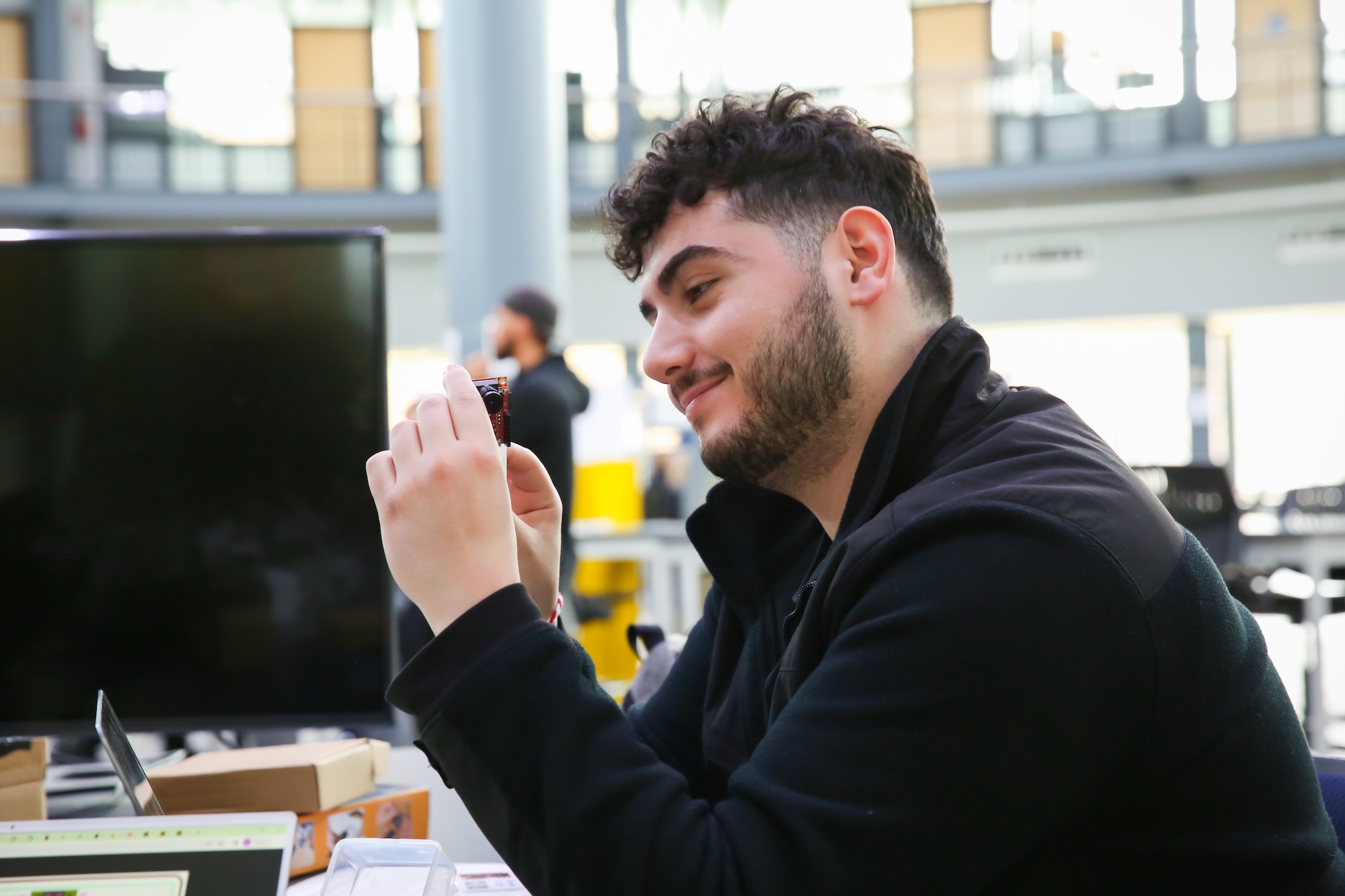 Person sitting at a desk in a modern office setting, smiling while looking at a smartphone.