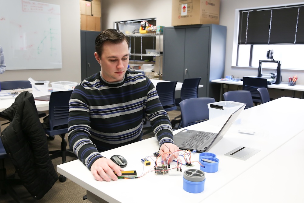 Person working on an electronic project with a laptop and various components on a table in an office environment.