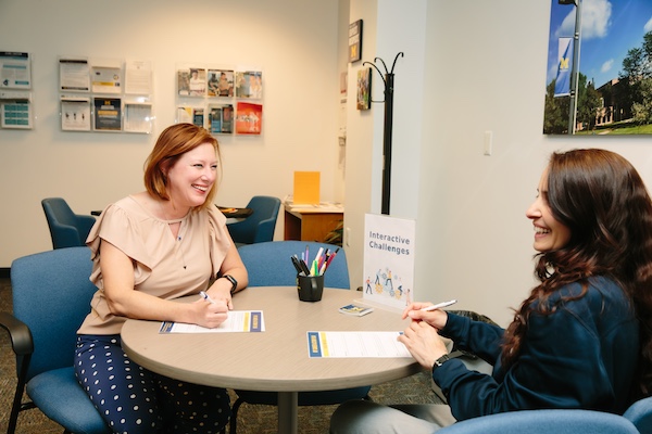 Smiling student and advisor meeting around a round table.