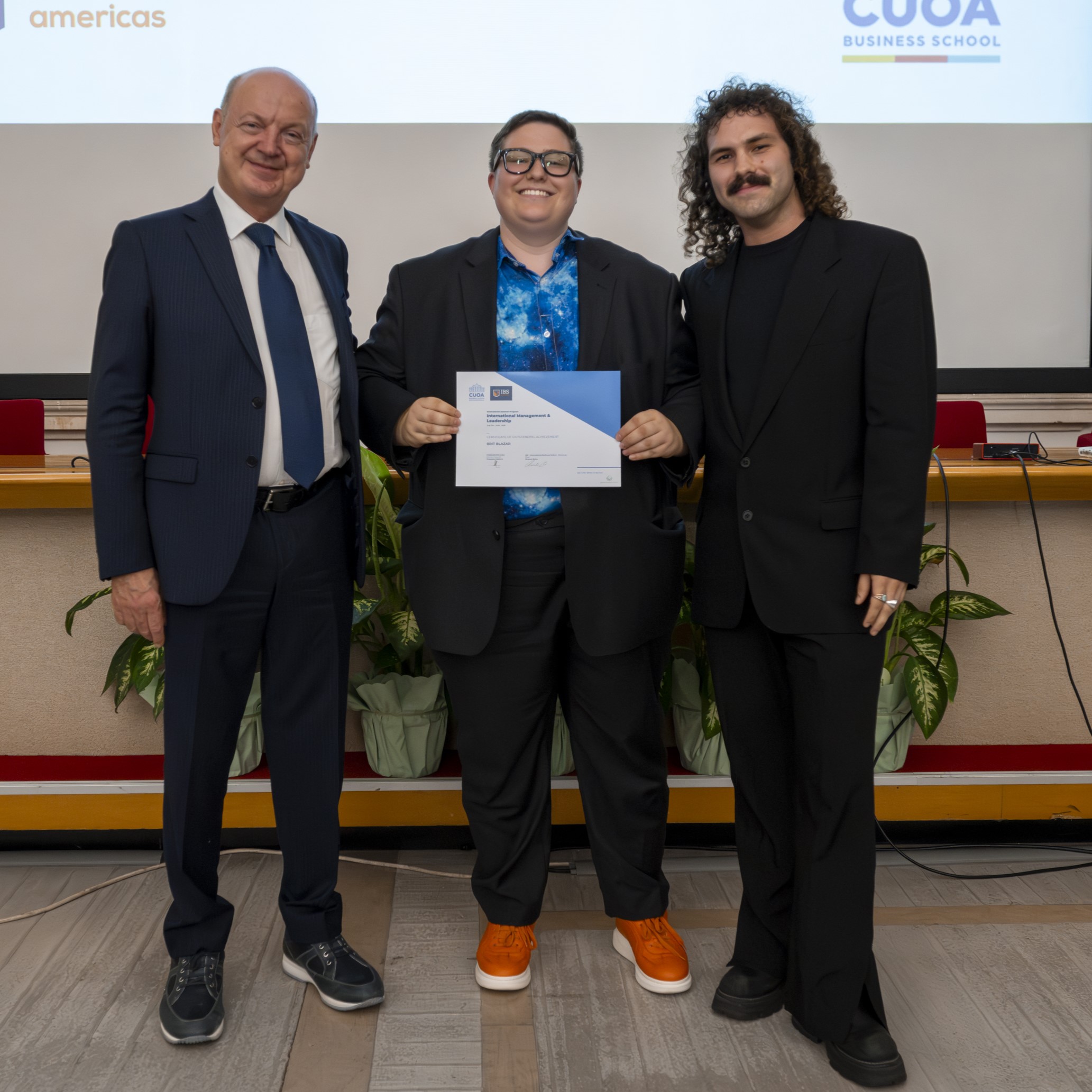 This image shows Brit Blazar holding their Certificate of Outstanding Achievement at a graduation ceremony at CUOA Business School for completing a study abroad program.