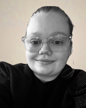 A black-and-white portrait of a person wearing clear-framed glasses and a dark top, smiling softly at the camera against a plain background.