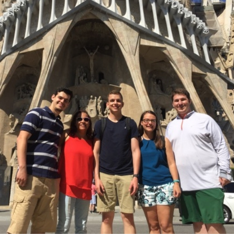 Group of five people standing together in front of an ornate cathedral facade on a sunny day.