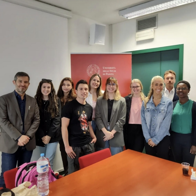 Group of students and faculty posing indoors at a university meeting room with a university banner in the background.