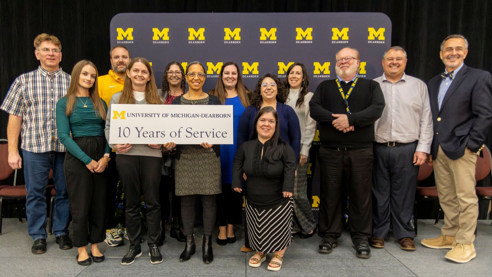 Staff receiving recognition for 10-years of service pictured on stage with Chancellor Grasso in front of a UM-Dearborn background