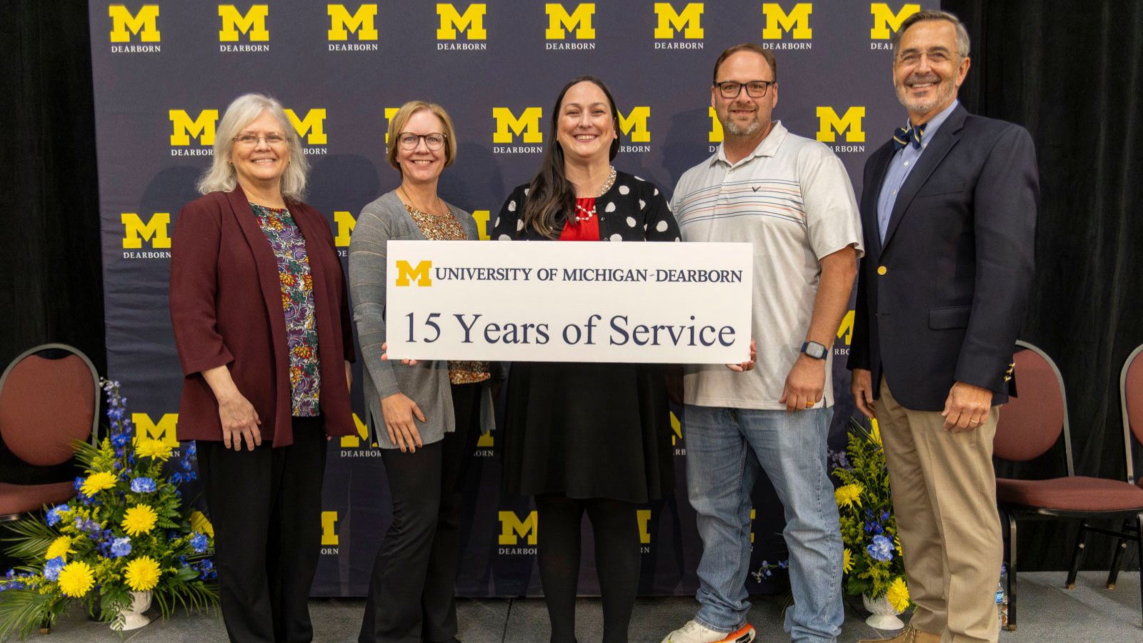 Staff receiving recognition for 15-years of service pictured on stage with Chancellor Grasso in front of a UM-Dearborn background