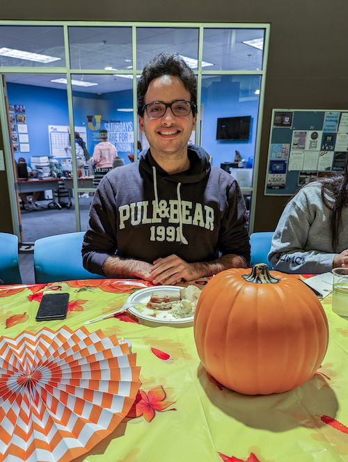 Graduate student Ata Kaboudi poses for a photo in front of holiday decorations at the 2022 UM-Dearborn Friendsgiving. 