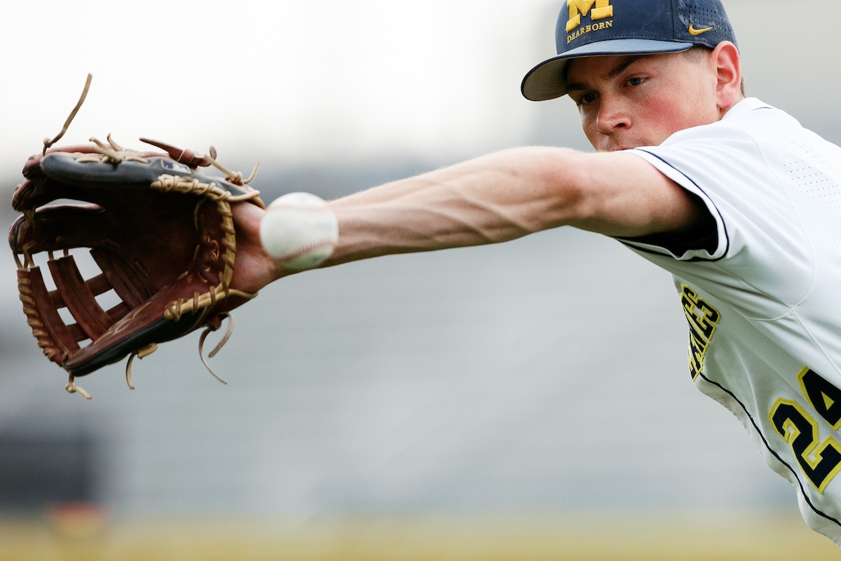 A male baseball player holds out his arm and the white ball is nearly in his baseball mitt.