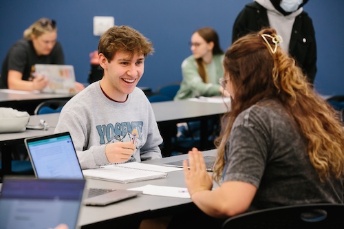 Two smiling students working together across a desk.