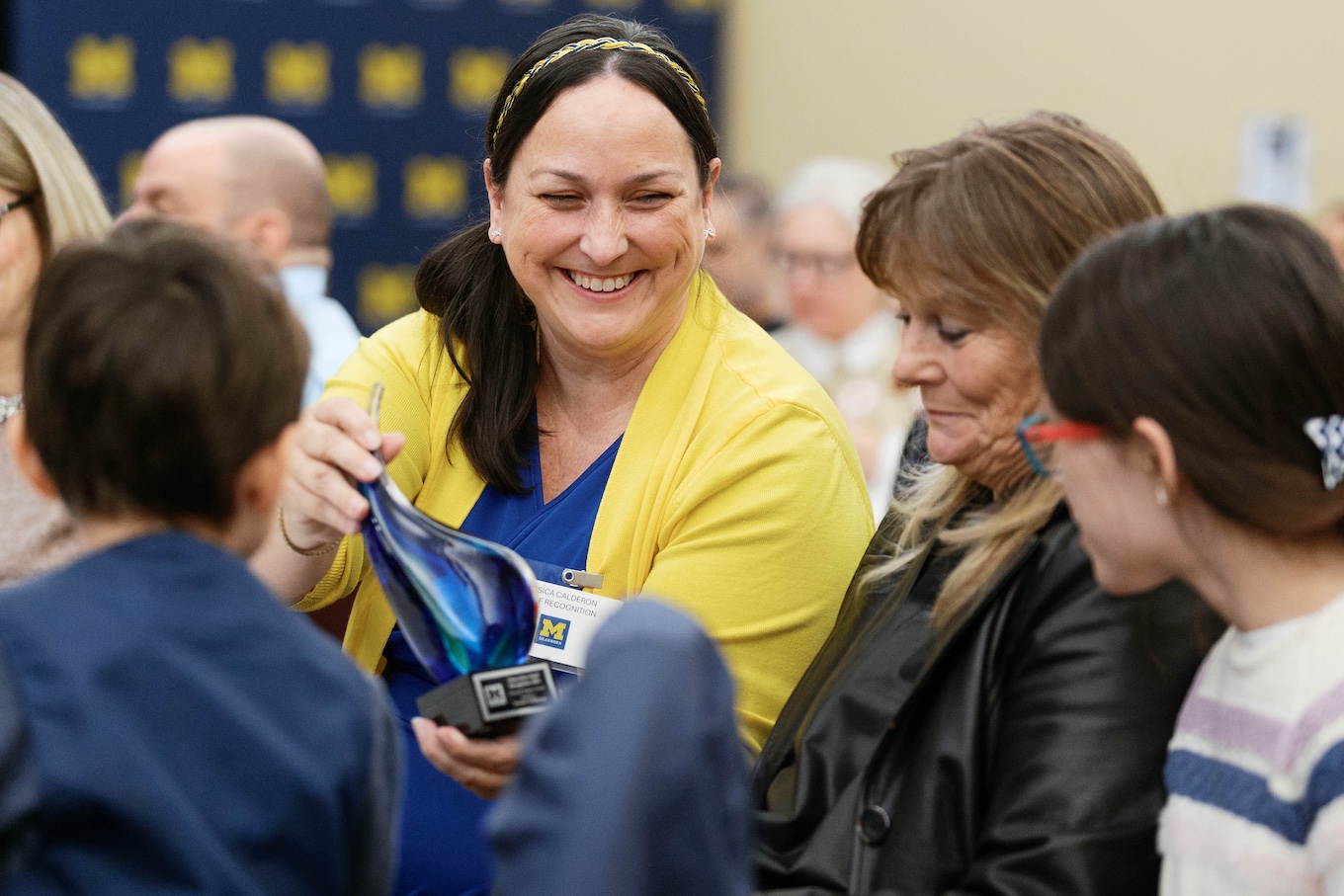 A smiling woman shows off her blue-tinted award trophy to her family.