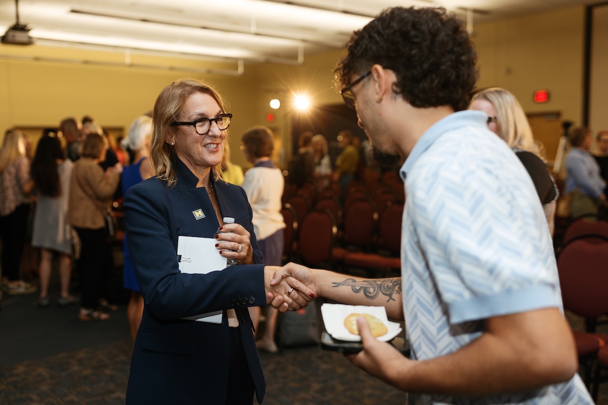 Scarlatta smiles and shakes hands with a young man who is holding a cookie after an event at UM-Dearborn.