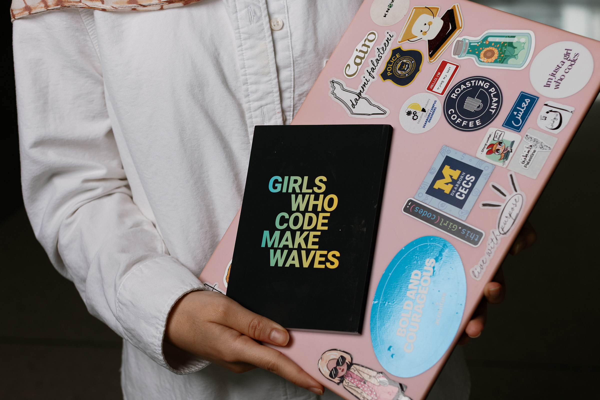 A student holds a pink laptop covered in stickers.
