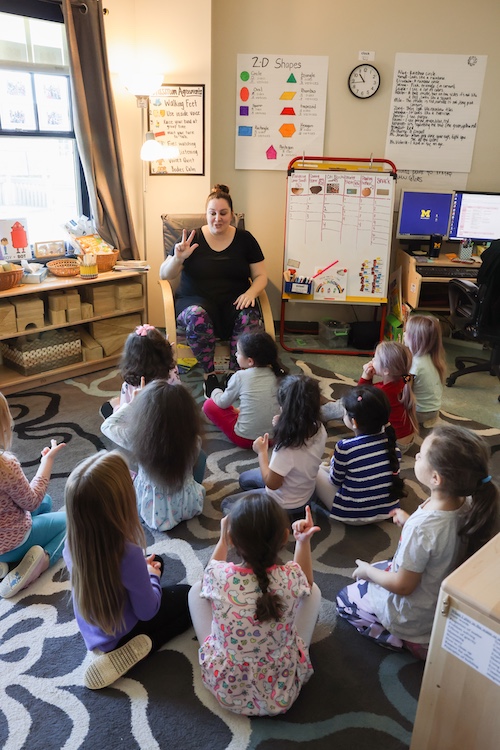 Student teacher leading younger students sitting on the floor.