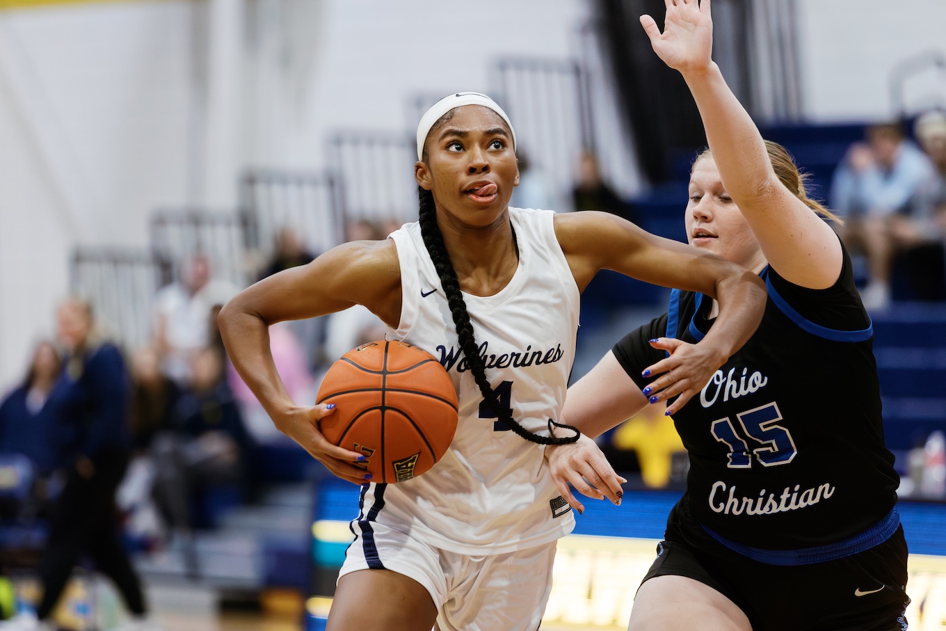 A female basketball player drives to the hoop with the ball cradled under her arm.