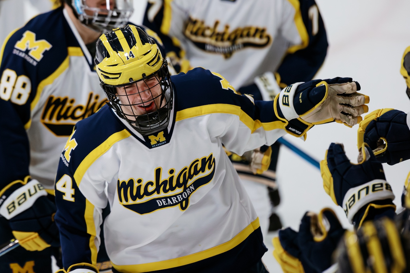 A smiling man with a hockey helmet on cheers with his teammates