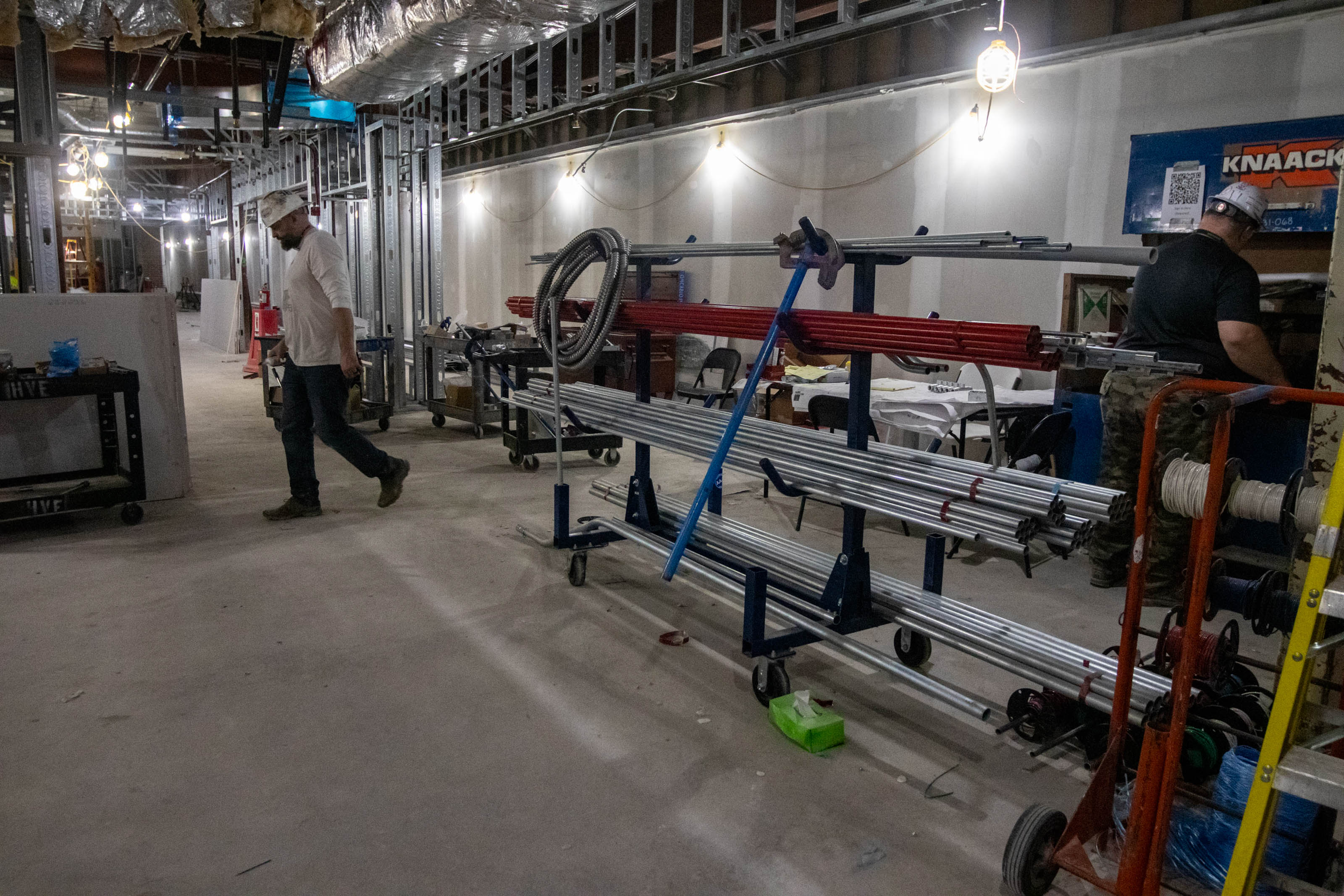 With stacks of metal tubing in the foreground, a worker in a hard hat walks in the first floor construction area of the Renick University Center, 