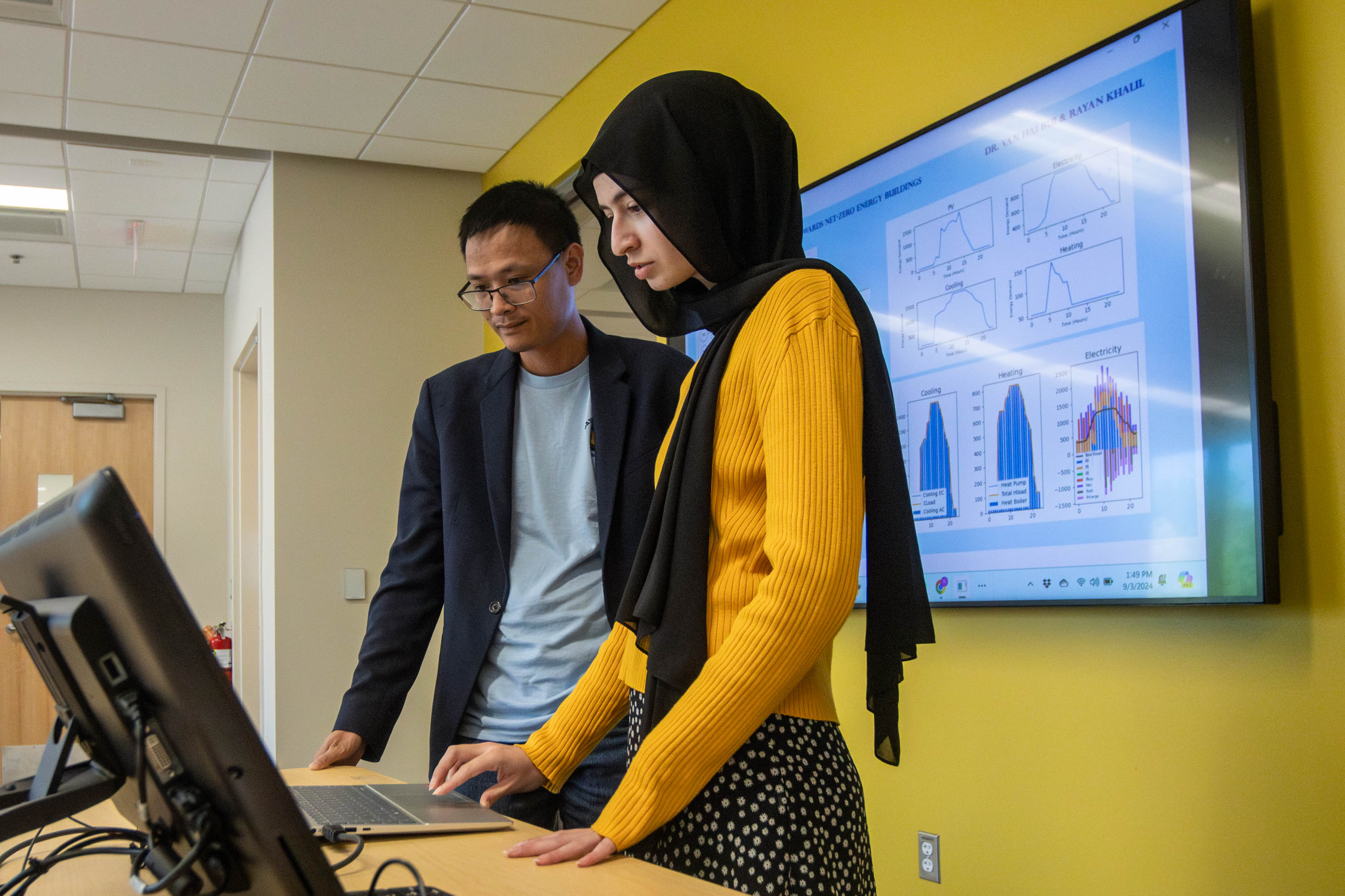 Student Rayan Khalil and Assistant Professor Van Hai Bui stand in front of a computer screen in Bui's research lab