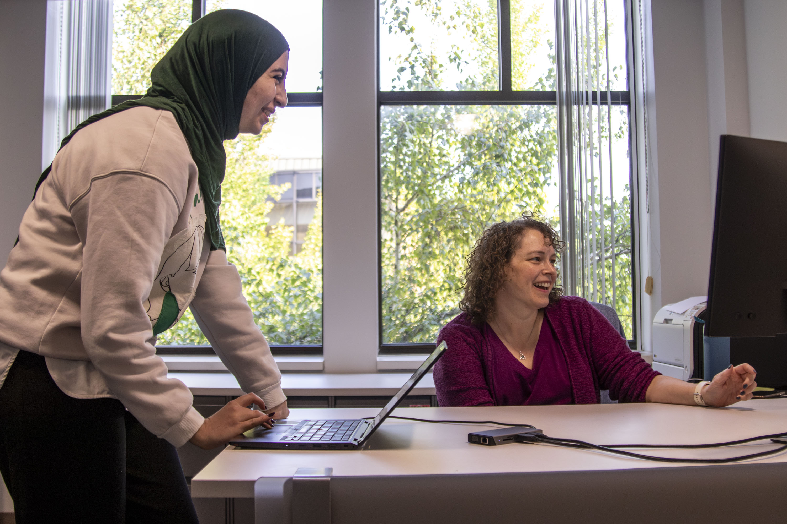 Student Sarah Caban and Professor Lisa Martin smile while working on computers in Martin's office