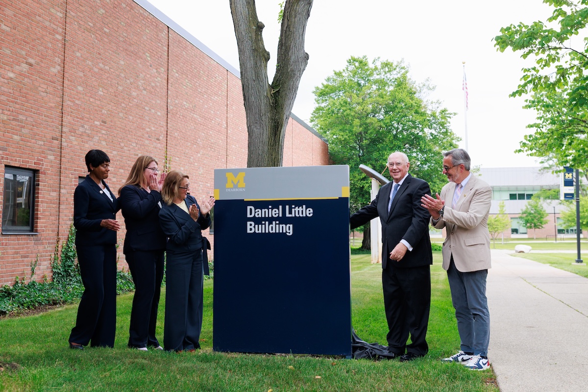 Five people gather around a sign that reads: Daniel Little Building. They are clapping in celebration of the new building's name.