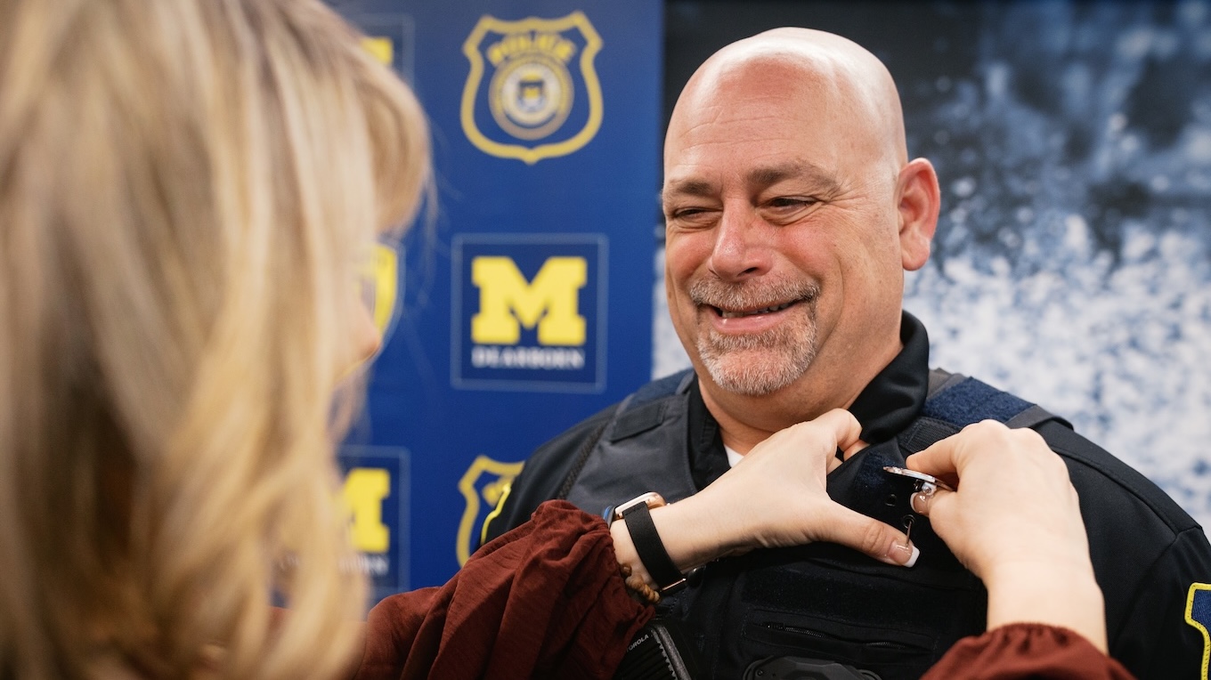 A man wearing a public safety officer uniform smiles as his police badge is pinned on his vest.