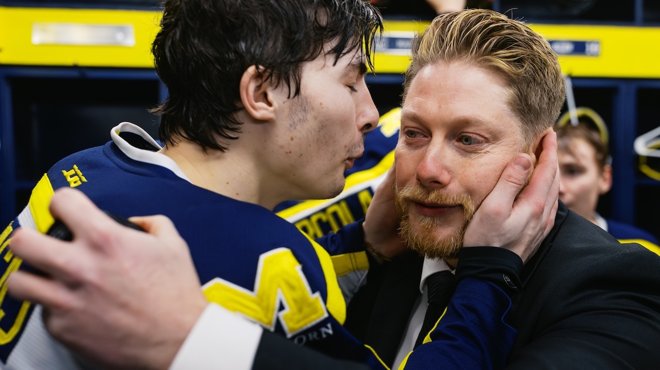 Two males — a coach and a UM-Dearborn men's ice hockey member embrace after a winning game. The coach has tears in his eyes because it was his last game coaching the team after 13 years.
