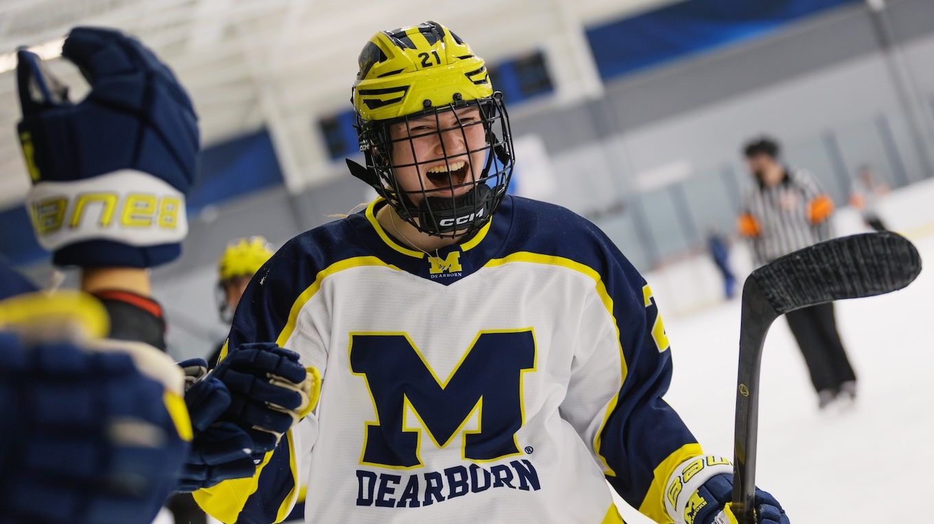 A UM-Dearborn Women's Ice Hockey member smiles and gives her team members hi-fives after scoring a goal.