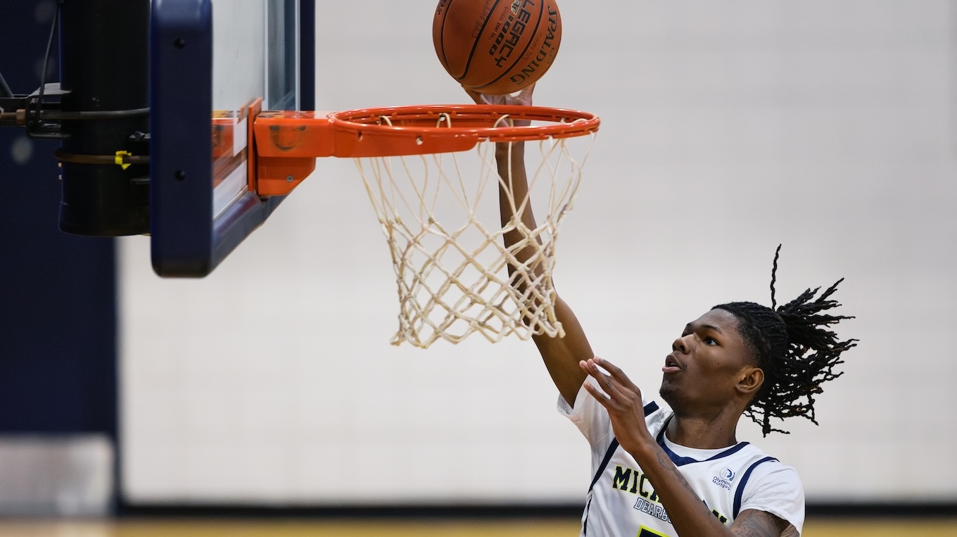 A male basketball player jumps up with the basketball and reaches the basketball hoop rim.