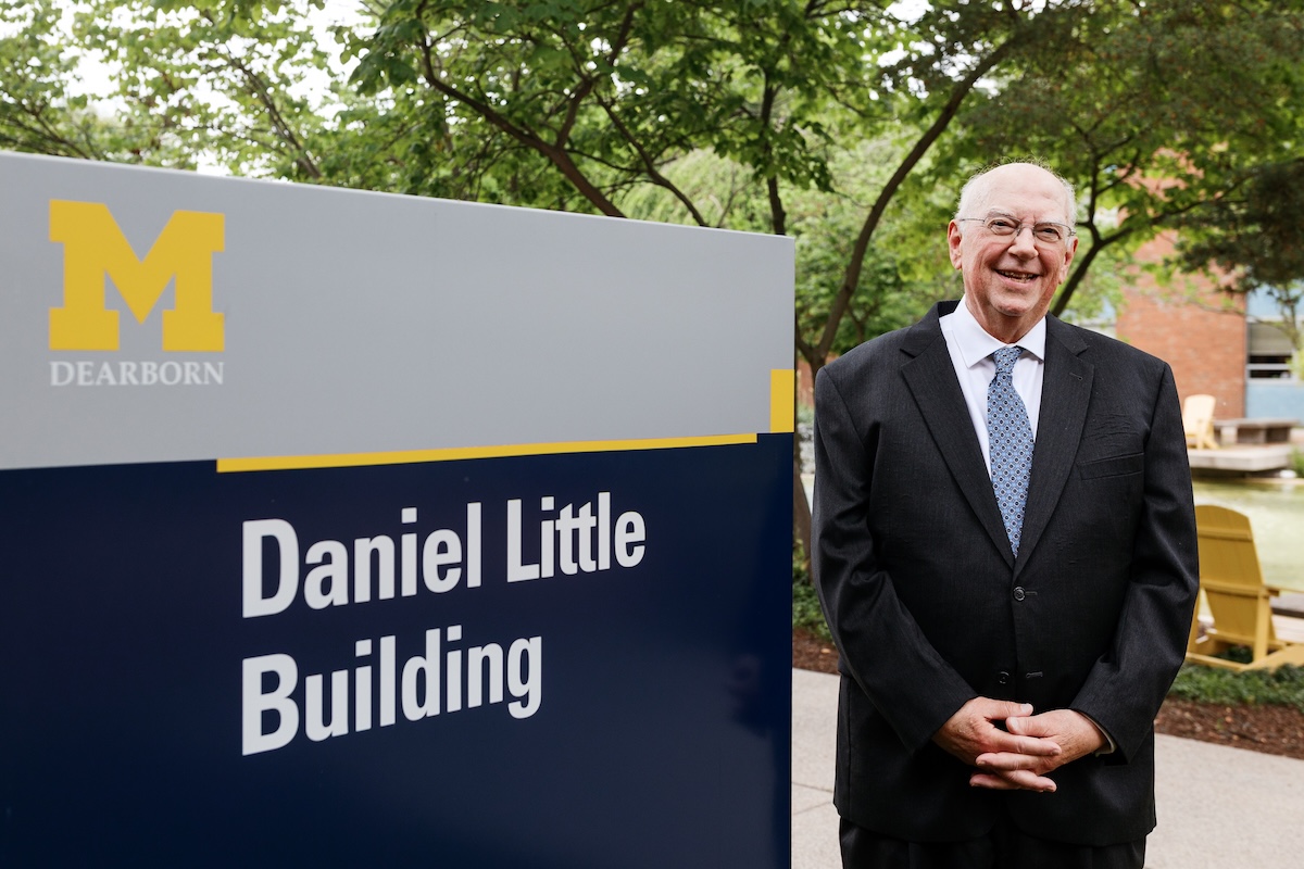 Daniel Little stands smiling next to a campus sign that reads "Daniel Little Building."