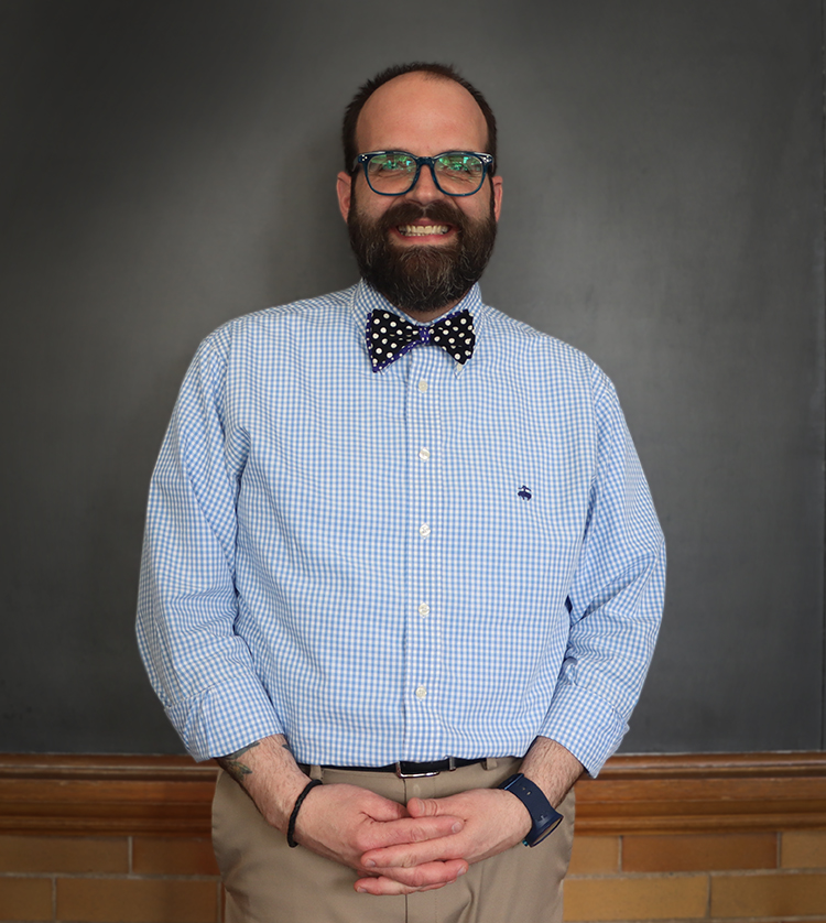 shot of Michael Gillespie in a blue plaid shirt with a polkadot bow tie in front of a grey back drop