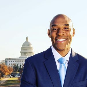 Person in a blue suit and light blue tie stands outdoors with the U.S. Capitol building in the background.
