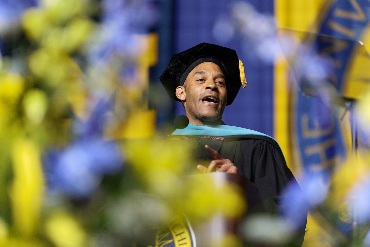 A photo of a man speaking at a podium. He is wearing a cap and gown.
