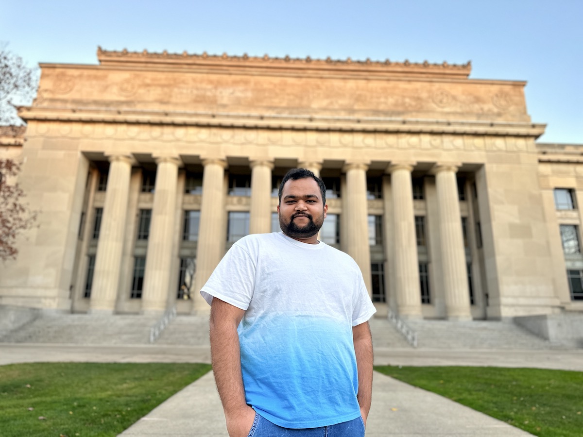 A portrait of UM-Dearborn student Bharat Kudachi standing in front of a stone building with Greek architecture.