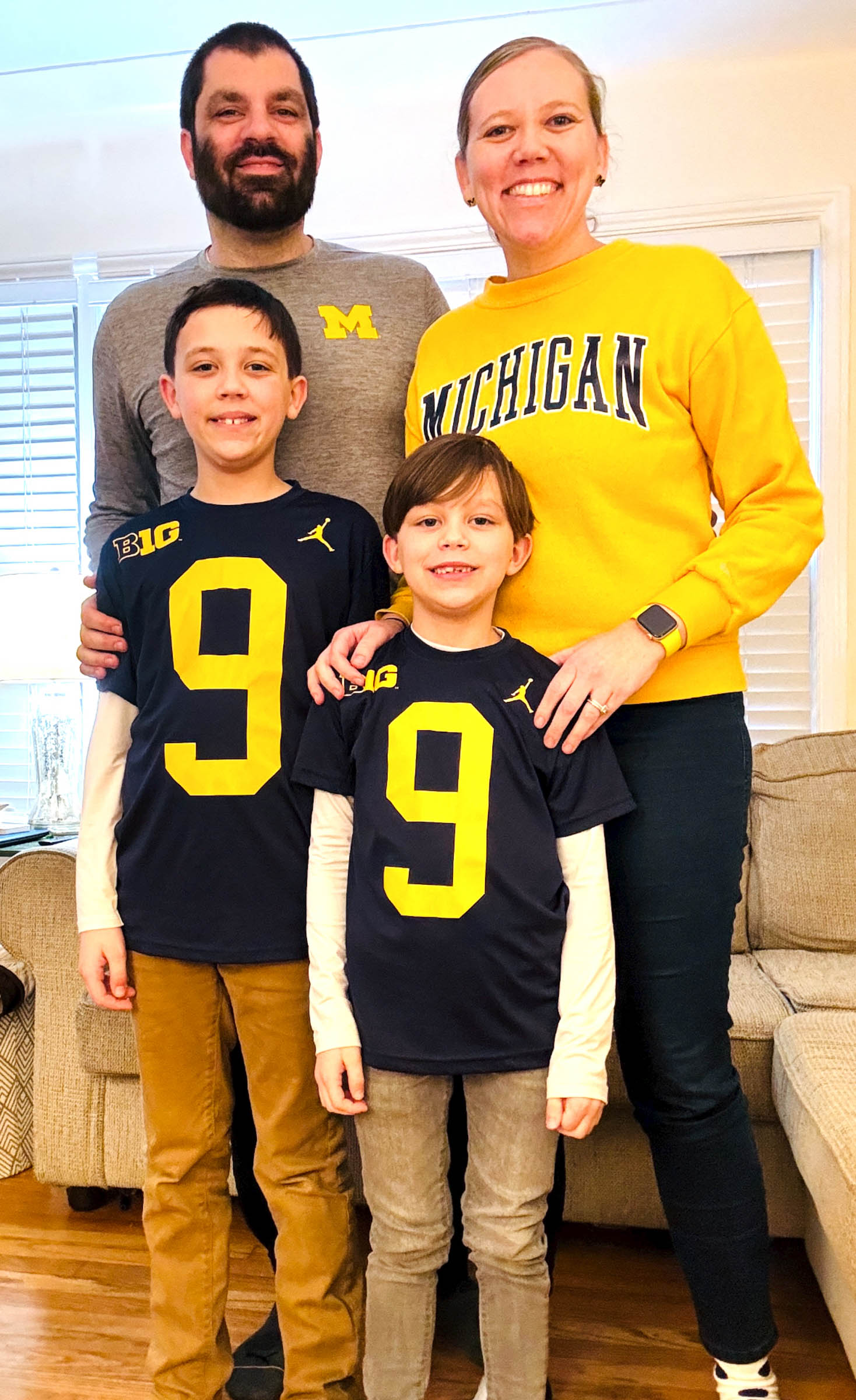 Emily Hutfloetz and Jesse Brady and their two kids pose for a family portrait wearing U-M gear