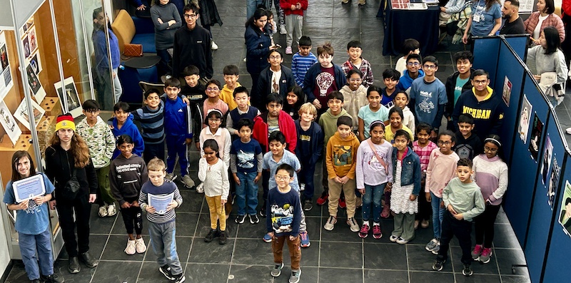 Overhead group photo of more than 50 students and organizers at UM-Dearborn.Participants gather indoors after the March 19 Math Kangaroo competition.Children stand together, some holding certificates, with faces intentionally blurred.