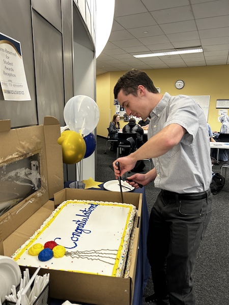 Student cutting a cake that reads Congratulations.