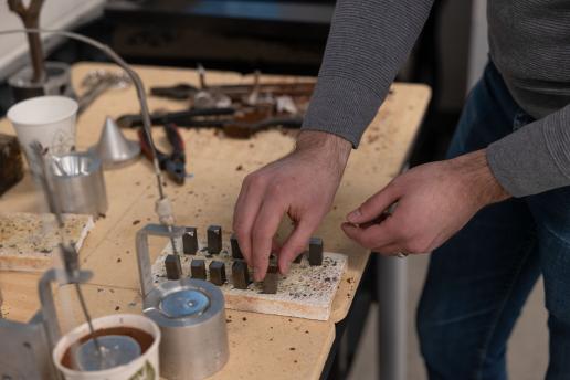 Person working with jewelry tools and materials on a workshop bench.