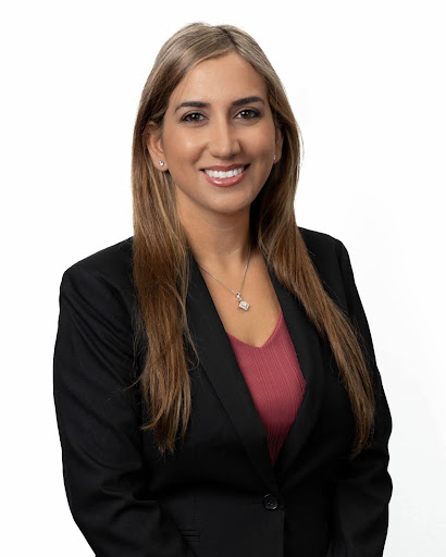 a smiling person with long brown/blonde hair wears a black blazer and red/pink shirt underneath