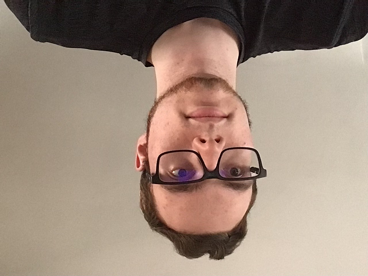 head-and-shoulders photo of a person wearing glasses and a dark shirt, with short hair and light facial hair, against a plain light-colored background.