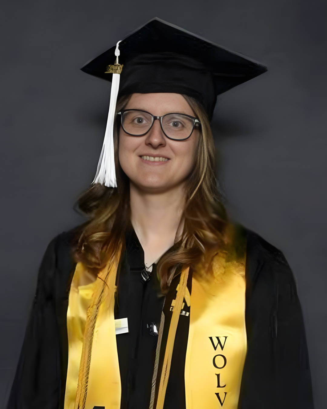 Woman with brown hair in glasses poses in her graduation cap and gown with stoles and cords