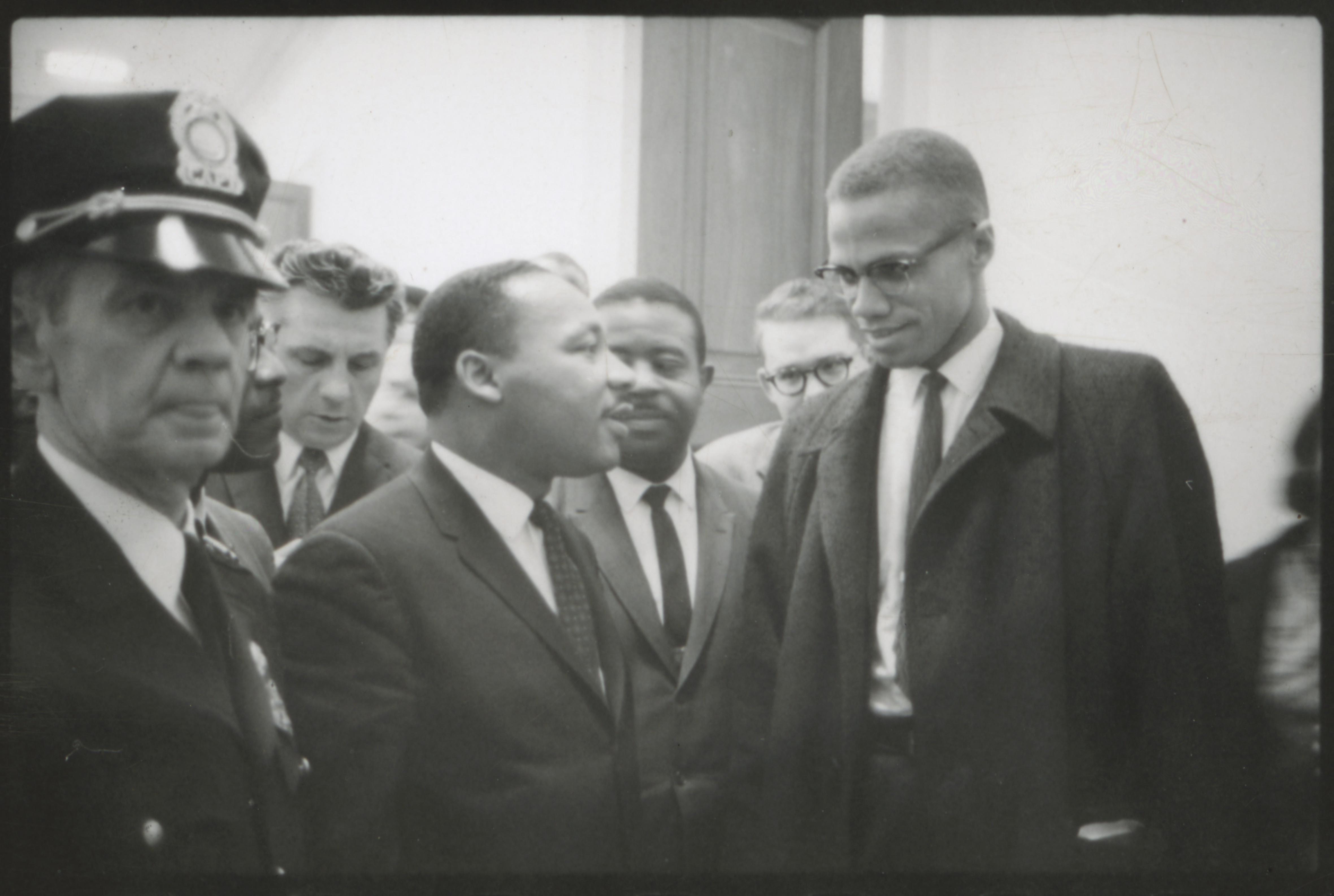 Martin Luther King and Malcolm X stand side by side surrounded by people in the hallway of the U.S. Capitol.