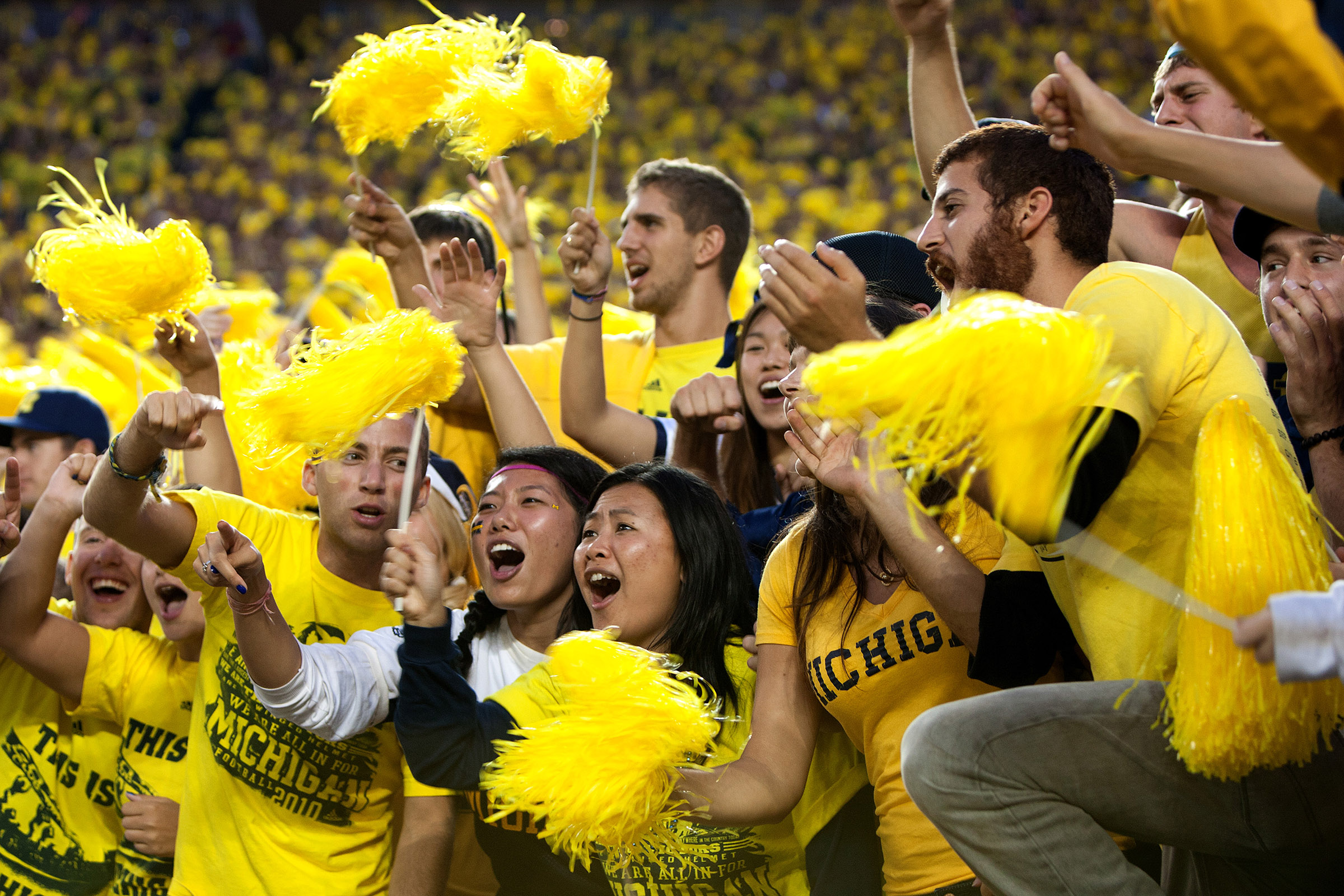 Wearing bright yellow shirts, students in the student section cheer at a U-M football game.