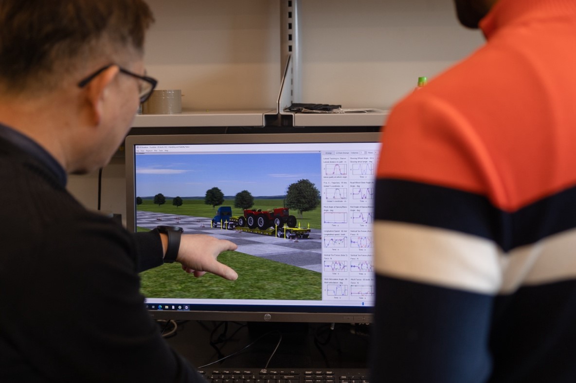 Two persons looking at a tractor model in a computer screen