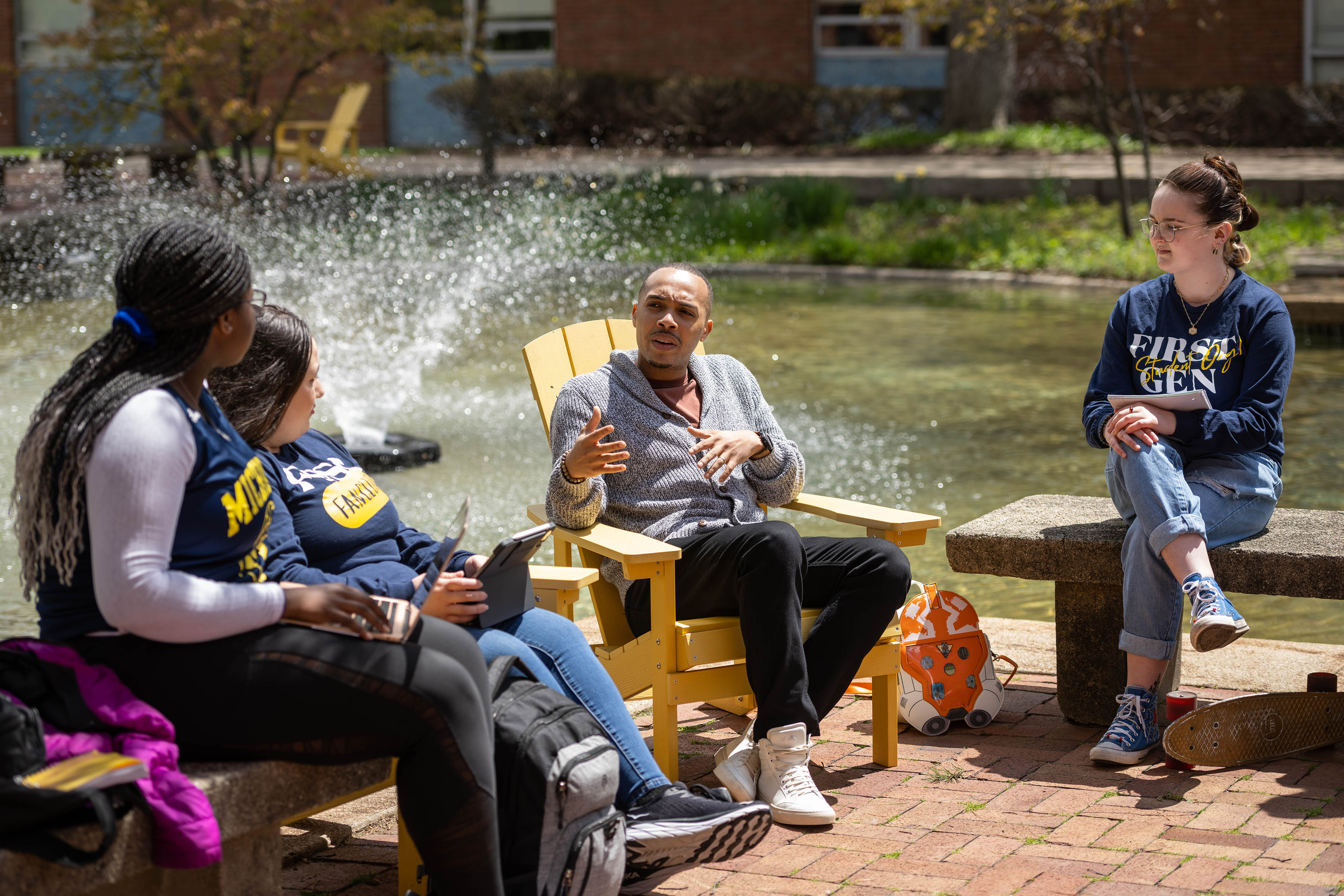 Alum Maurice Taylor sits and talks with students next to Chancellor's Pond with the fountain in the background.